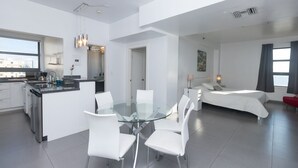 A modern hotel room with a glass dining table, white chairs, a kitchenette, a separate bedroom with a bed, and a city view. - 701 Ocean View Hollywood Beach (Hollywood)