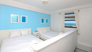 Een hotelkamer met twee bedden, een klein tafeltje, een nachtkastje en een raam met uitzicht op zee.