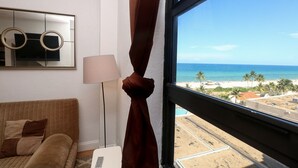 Een kamer met uitzicht op het strand, een bank, een lamp en een spiegel met zonnebril.