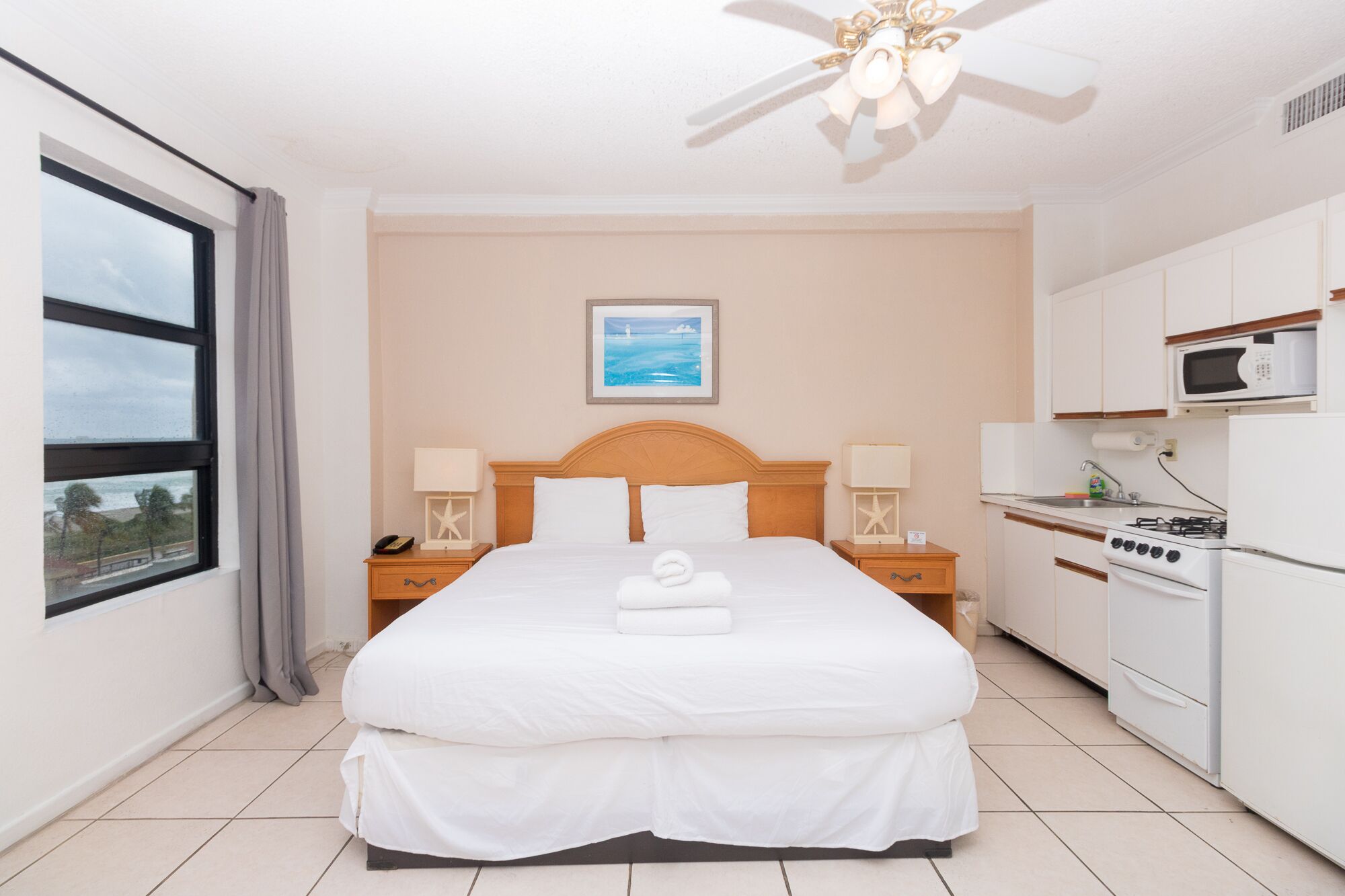Habitación de hotel con cama, mesita de noche, escritorio, kitchenette y vista al mar.