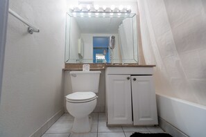 A small bathroom with a toilet, a vanity with a mirror, and a shower area.