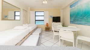 A hotel room with a bed, a desk, a chair, a television, a ceiling fan, a window with a view of the ocean, and a painting of a wave. - 703 Ocean View Hollywood Beach (Hollywood)