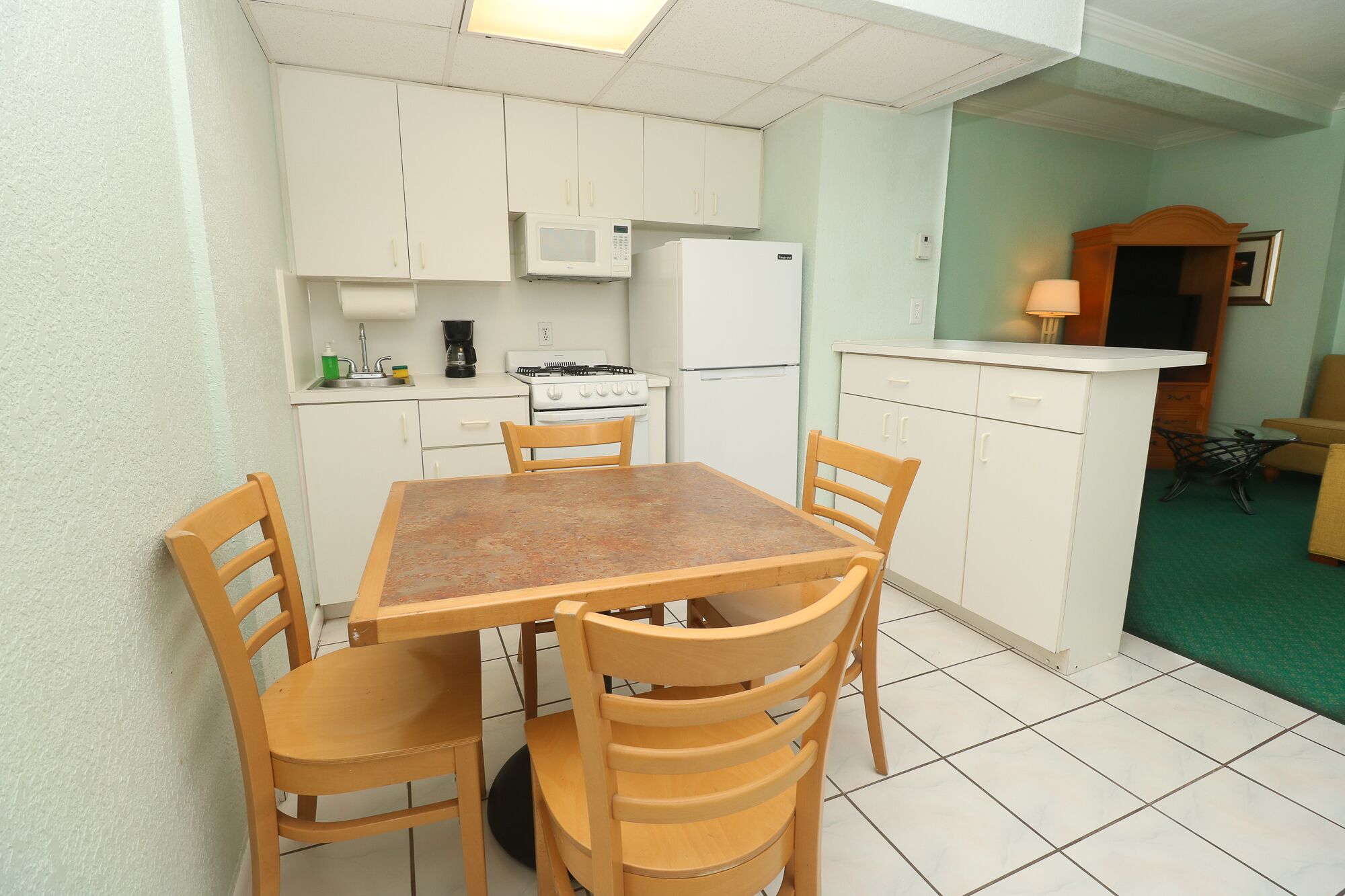 A compact kitchen with white cabinets, a stove, a microwave, and a refrigerator. There is a wooden table with chairs.