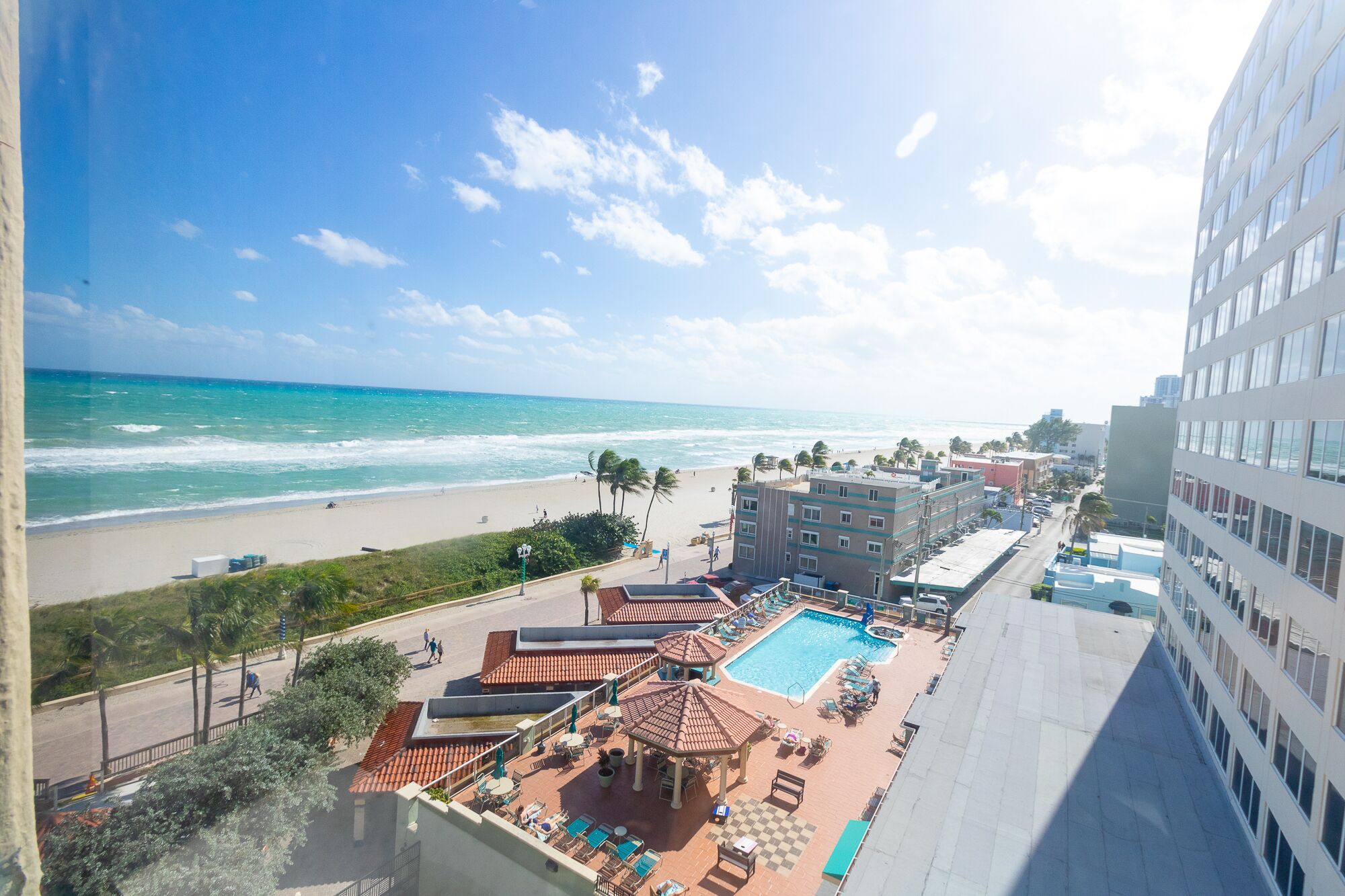 Un hotel con piscina en la azotea, vistas a la playa y zona de estacionamiento.
