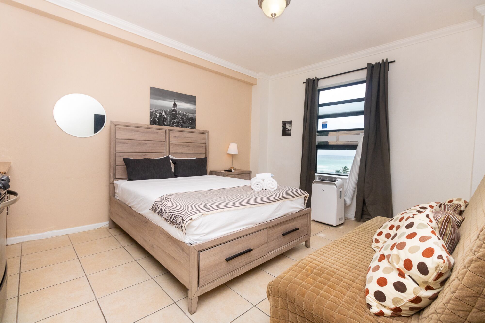 Une chambre avec un lit en bois, une table de chevet avec une lampe, une fenêtre avec des rideaux et une vue sur la mer.