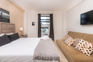 A hotel room with a bed, a sofa, a TV, a window with curtains, and a picture of a cityscape. - 707 Partial Ocean Hollywood Beach (Hollywood)