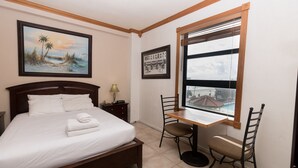 Een hotelkamer met een bed, een bureau met stoel, een raam met uitzicht en twee afbeeldingen in lijsten aan de muur.