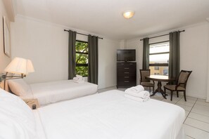 Ett hotellrum med två sängar, en TV, ett skrivbord med stolar och ett fönster med gardiner.