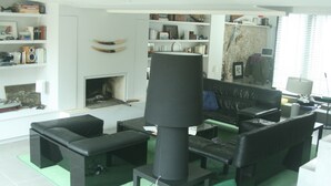 A modern living room with a fireplace, black leather furniture, and a bookshelf filled with books and decorative items. - Character house downtown, quiet street, near castle, harbor (Noirmoutier-En-L'île)