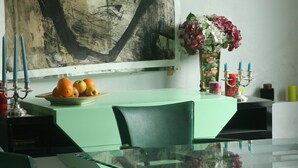 A dining area with a glass table, green chairs, a vase with flowers, and a large abstract painting on the wall. - Character house downtown, quiet street, near castle, harbor (Noirmoutier-En-L'île)