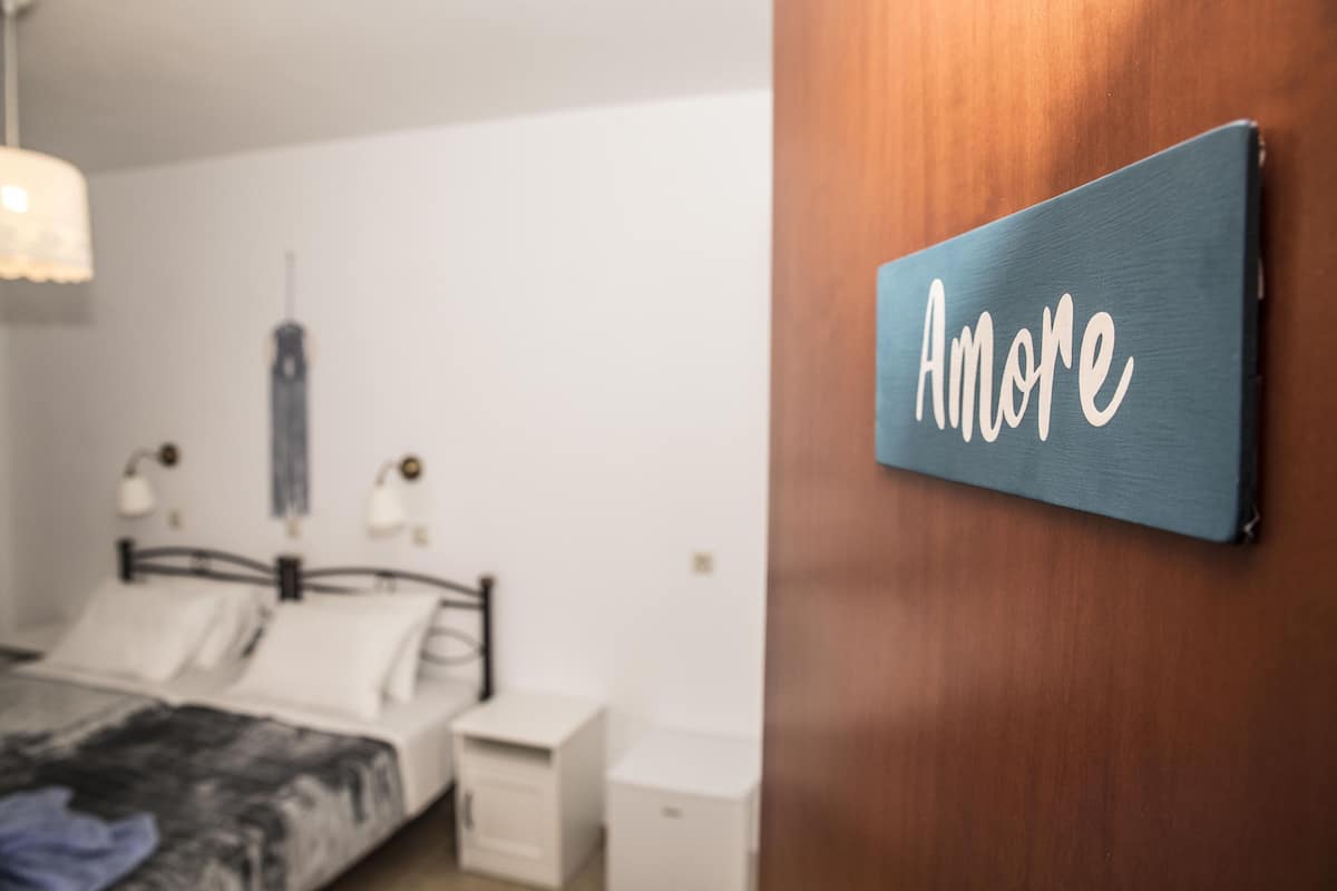 Une chambre à coucher avec un lit, des tables de chevet et un panneau mural sur lequel on peut lire le mot « Amore ».