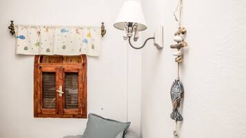 Een kamer met een houten raam, een grijze bank, een witte muur, een lamp en een decoratie aan de muur.