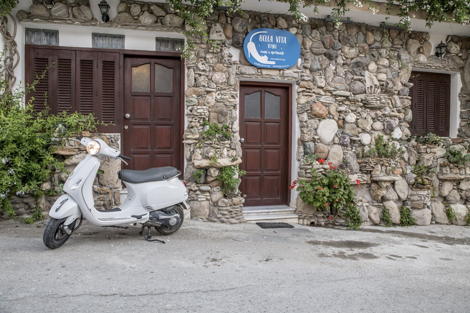 A stone building with a sign for 'Bella Vita Style' and a white scooter parked in front.
