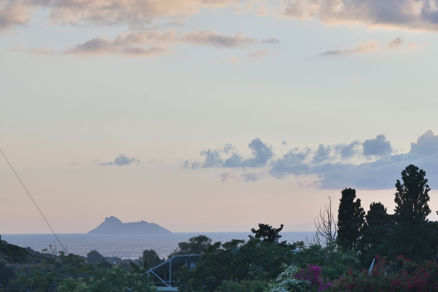A coastal landscape with a mountain in the distance, surrounded by greenery and trees.