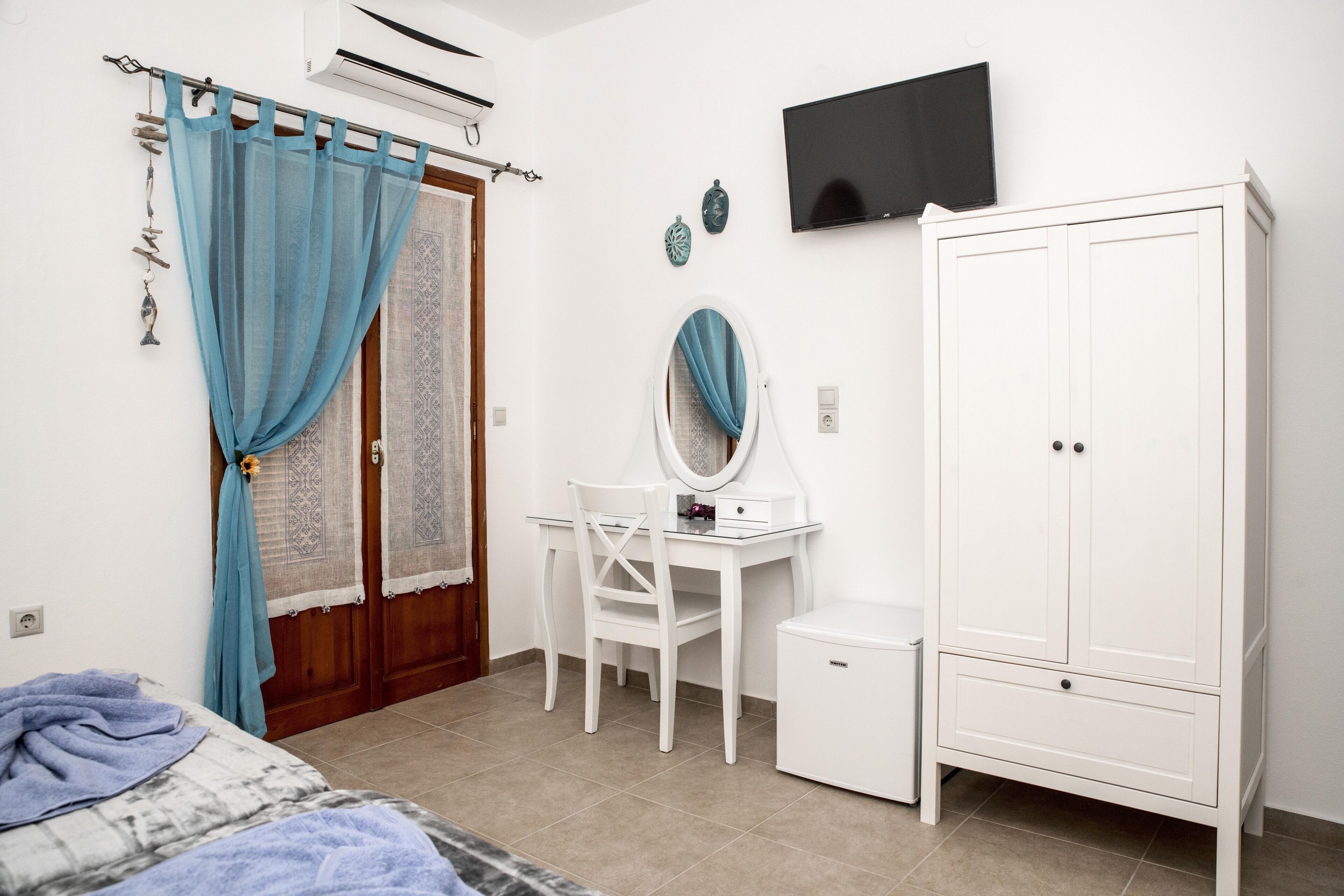 A bedroom with a bed, a desk with a chair, a wardrobe, and a television on the wall.