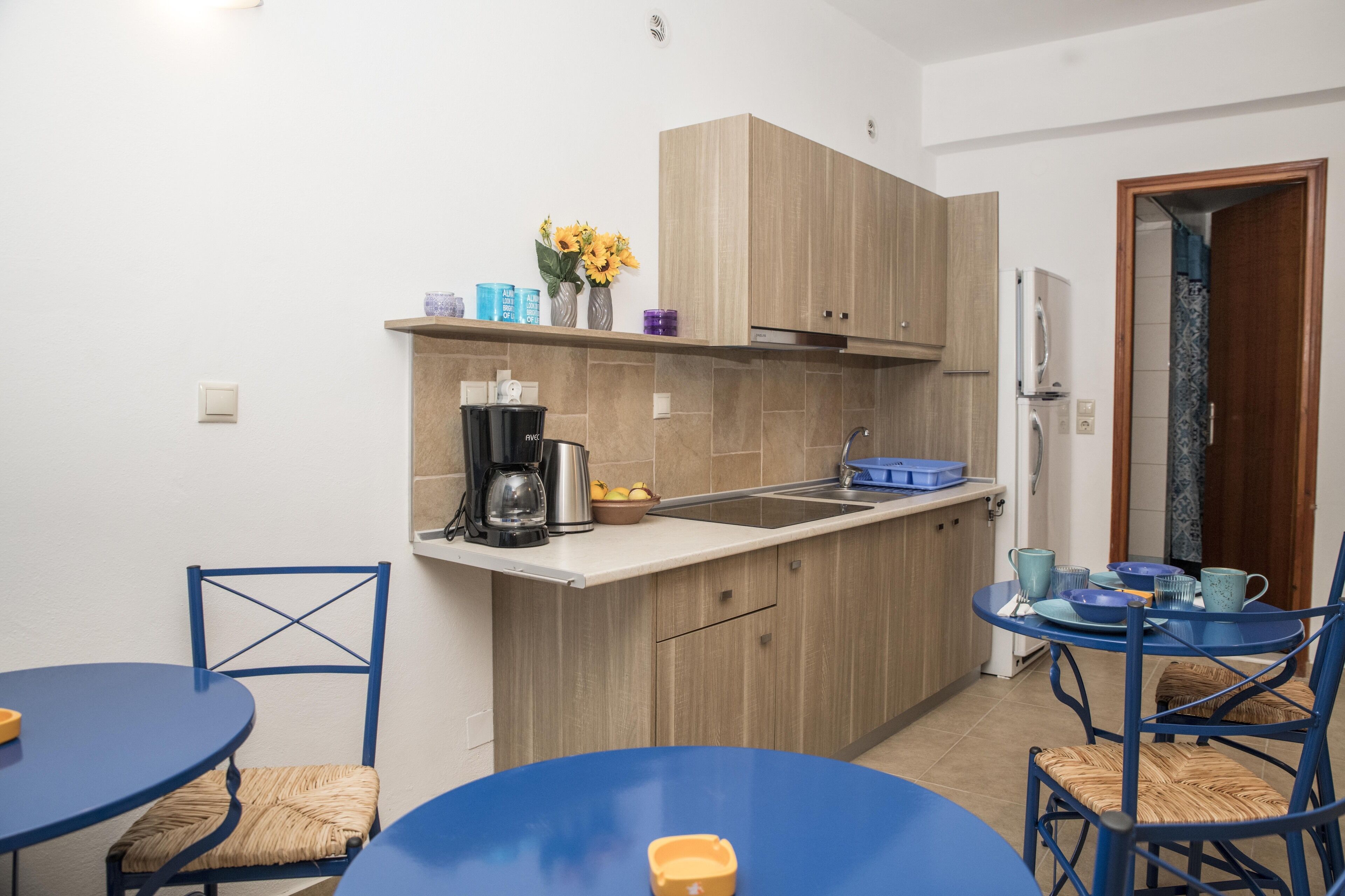 A compact kitchen with wooden cabinets, a sink, and a dining area with blue tables and chairs.