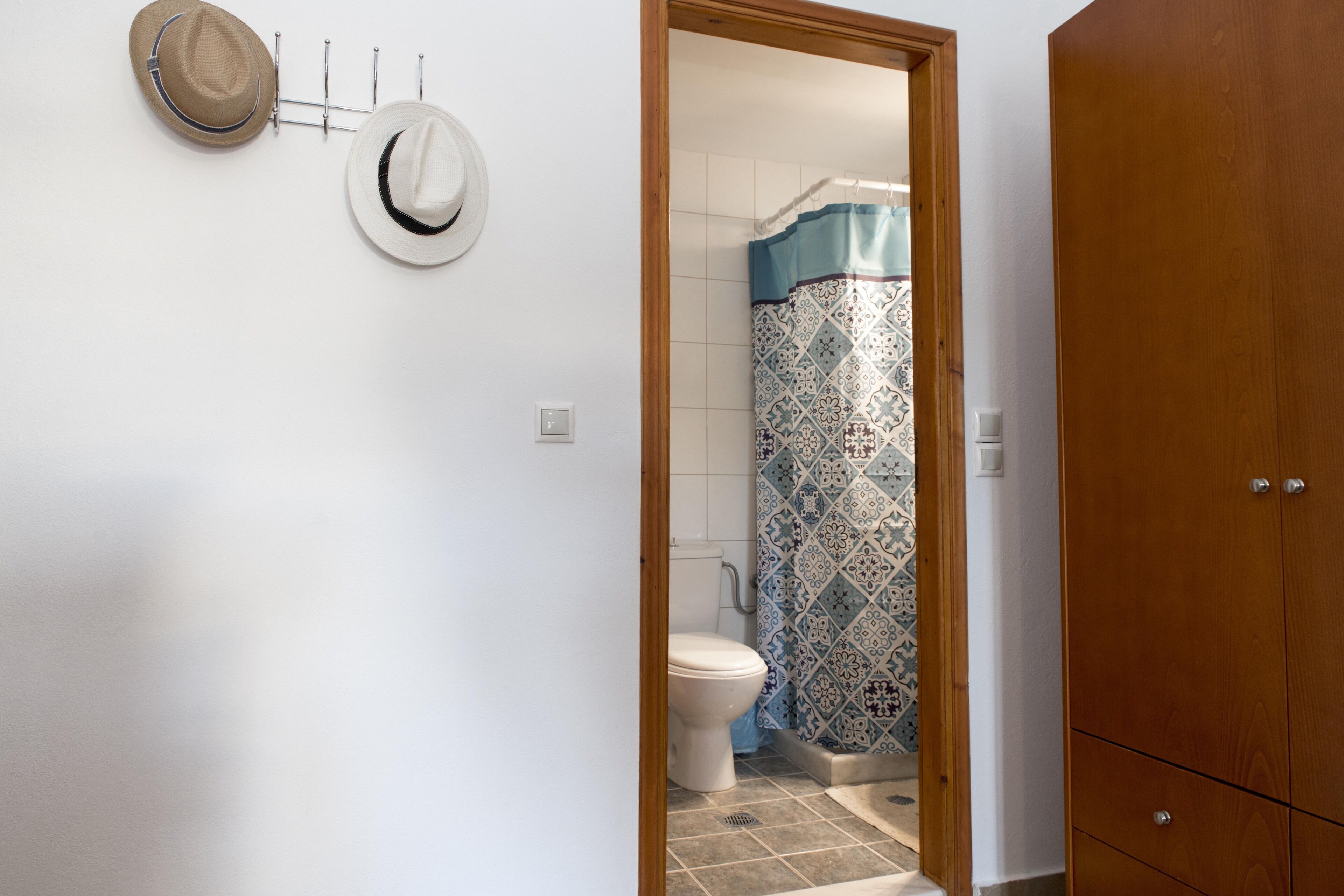 A bathroom with a toilet, shower curtain, and wooden wardrobe.