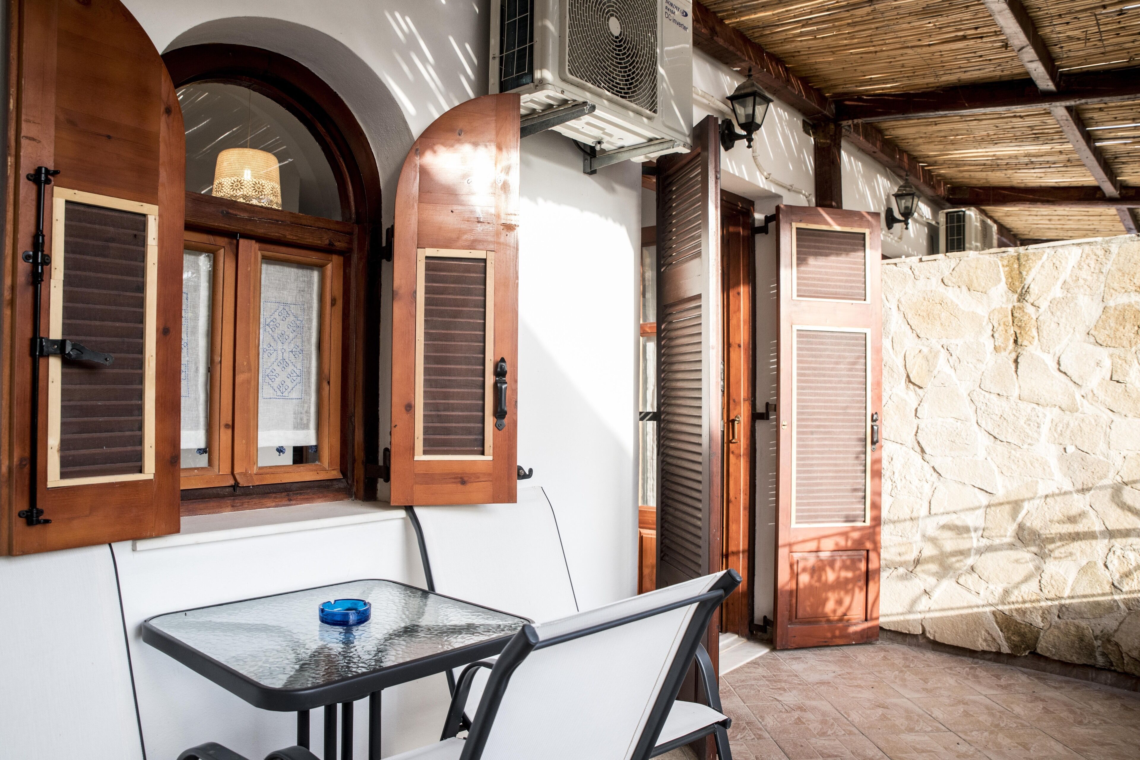 A patio area with a table and chairs, a window with shutters, and a stone wall.