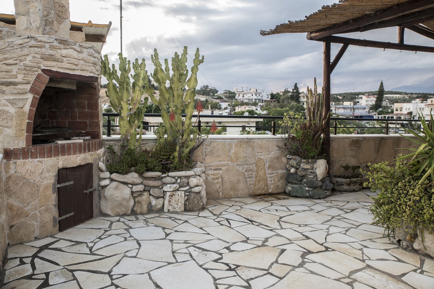 A stone patio with a brick oven, cacti, and a view of buildings in the background.