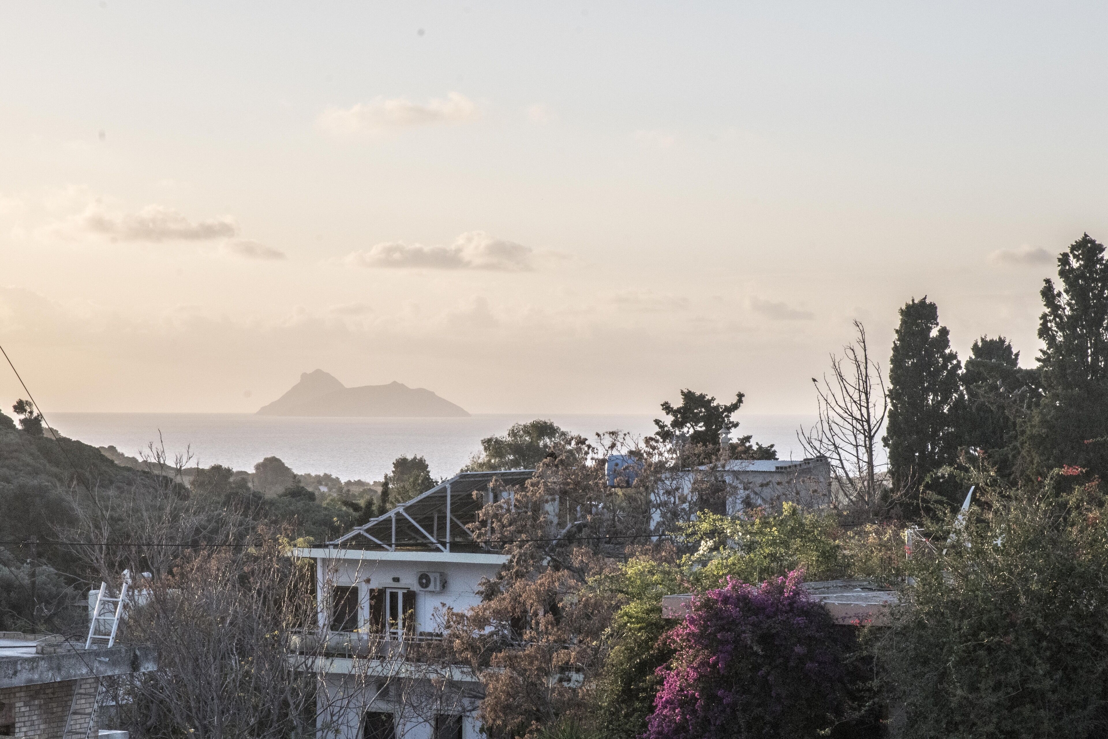 Blick auf die Küste mit einem Haus und Bäumen im Vordergrund, einem Berg im Hintergrund und dem Meer.