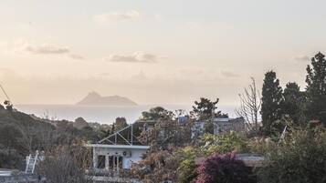 Blick auf die Küste mit einem Haus und Bäumen im Vordergrund, einem Berg im Hintergrund und dem Meer.