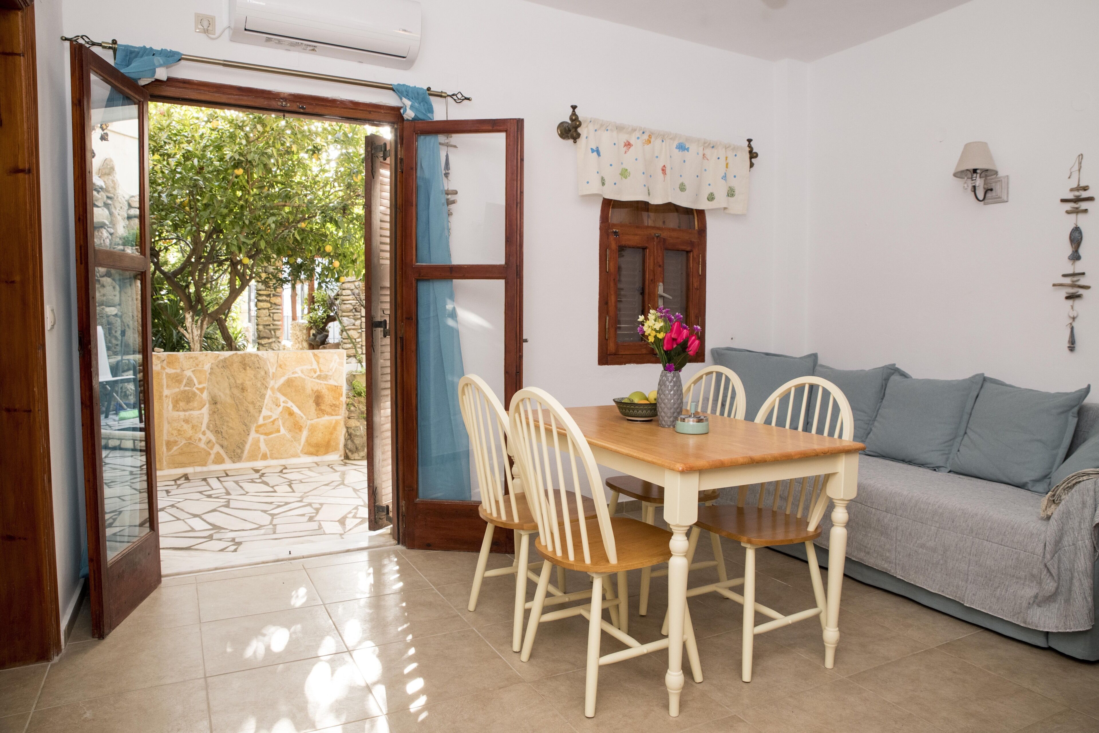 A dining area with a table and chairs, a sofa, a window with curtains, and a stone wall.