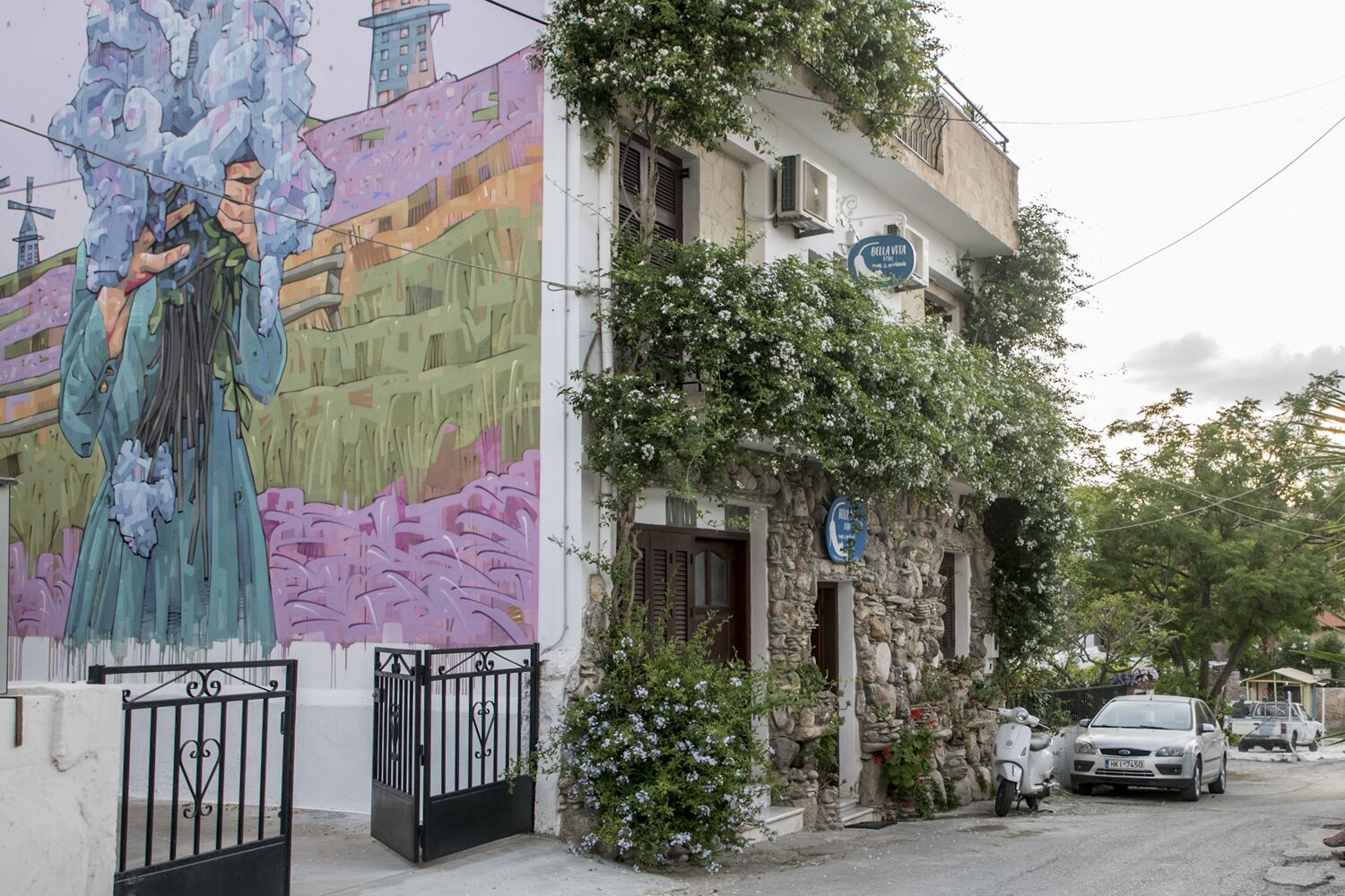 Un edificio con un mural a la izquierda, fachada de piedra y un letrero que dice 'Bella Vita'.