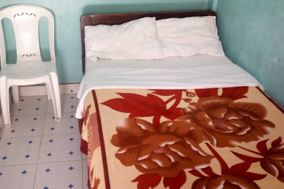 A small room with a bed, a white plastic chair, and a tiled floor.