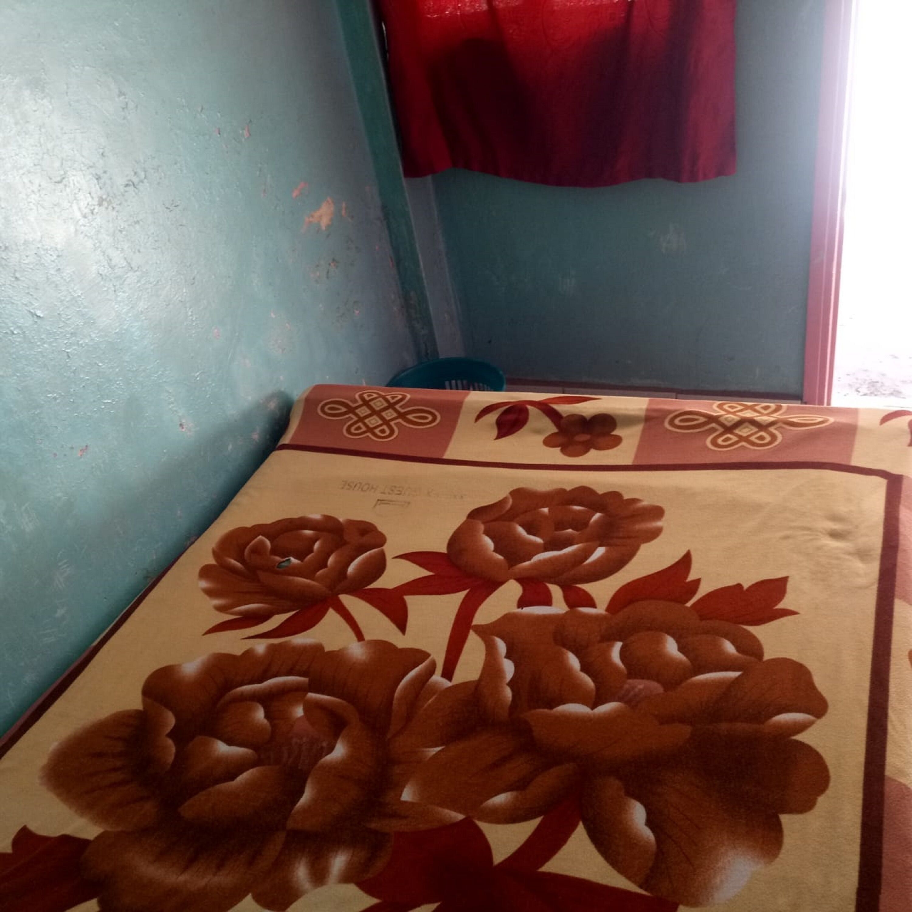 A bed with a floral-patterned bedspread, a blue wall, and a red curtain.
