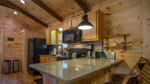 A wooden cabin interior with a kitchen featuring a granite countertop, a black refrigerator, a microwave, a coffee maker, and a sink. - Creekside Log Cabin in Pisgah Forest (Pisgah Forest)