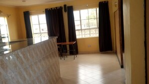 A spacious room with a tiled floor, a small table, chairs, and a window with curtains. - Meris Lodge (Naivasha)