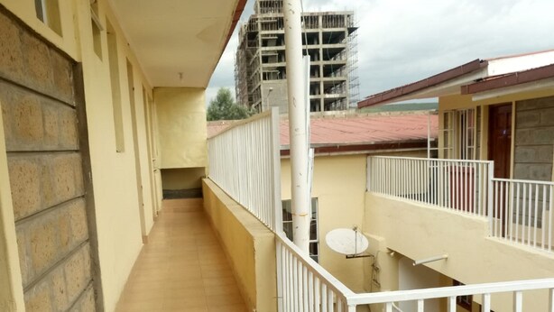 A corridor with a tiled floor leading to a balcony with white railings. - Meris Lodge (Naivasha)