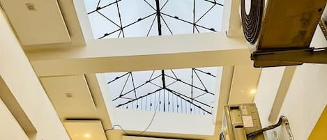 A multi-level interior with a geometric ceiling design, visible ductwork, and a central air conditioning unit.