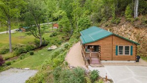 Een chalet met een groen dak, omgeven door een bebost gebied met een grindpad er naartoe.