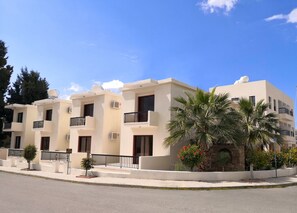 A row of modern, two-story buildings with balconies, air conditioning units, and a clear blue sky.