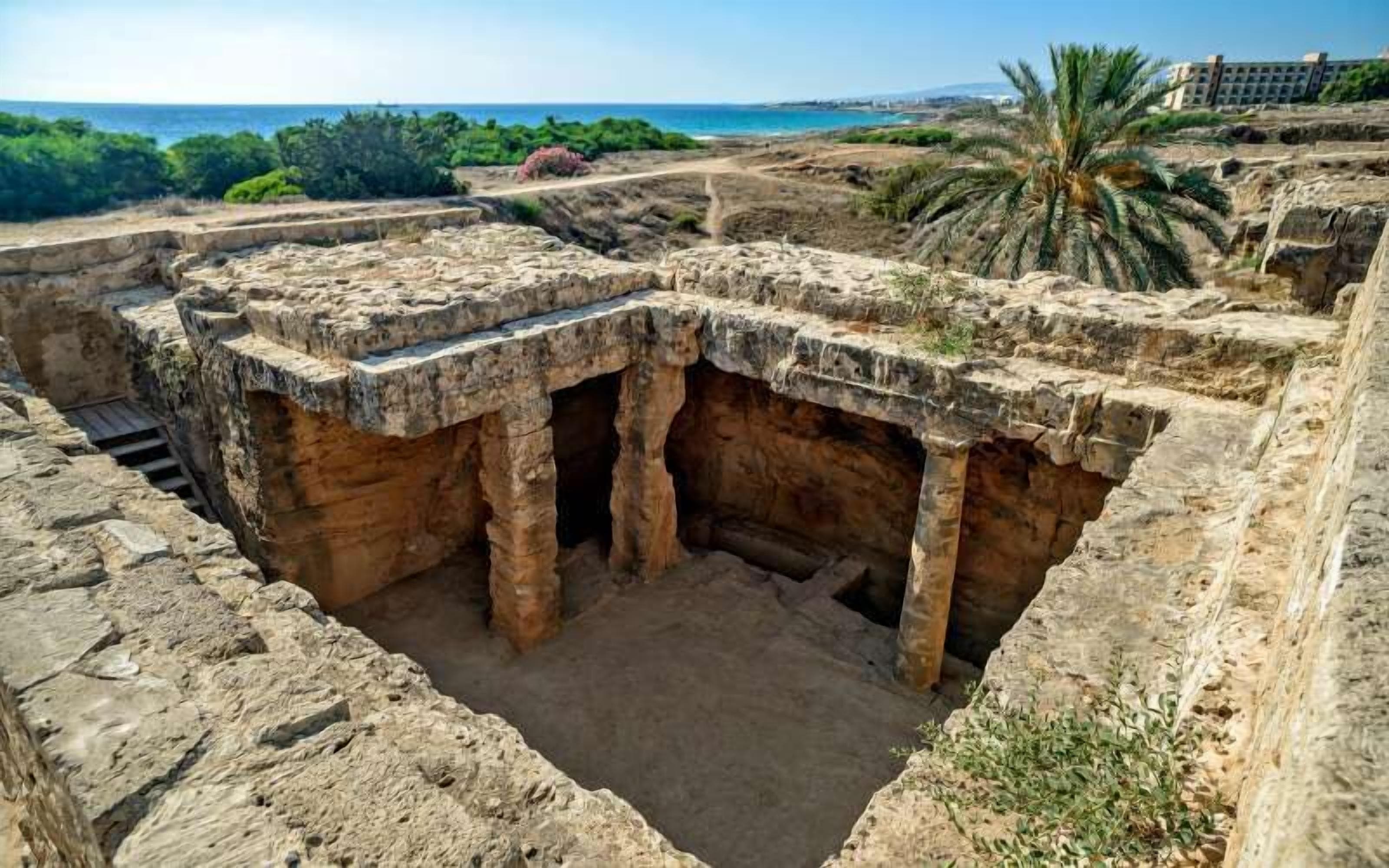 An archaeological site with ancient stone structures and a view of the sea.