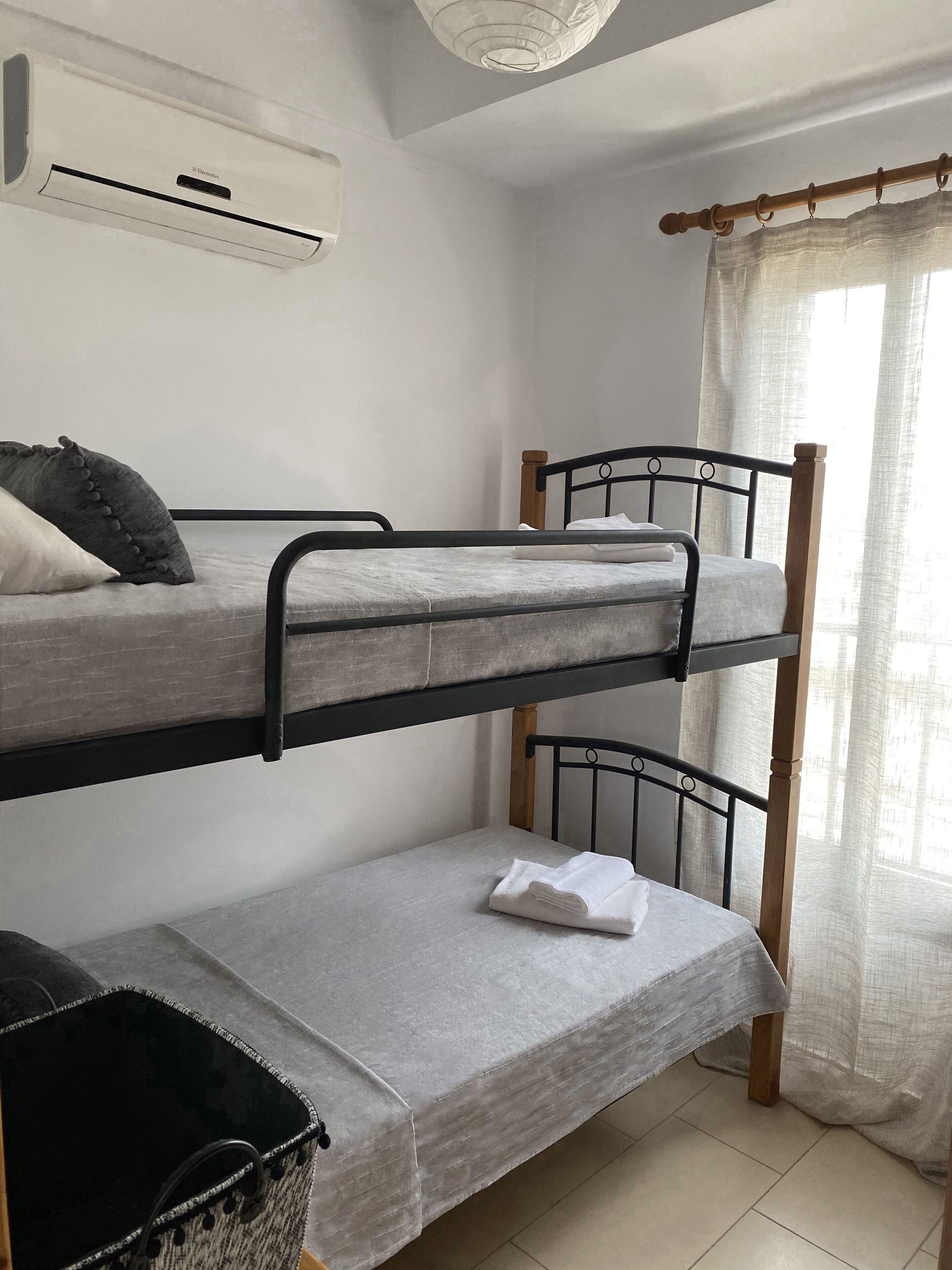 A bunk bed room with a ceiling air conditioner, a window with sheer curtains, and a small basket on the lower bunk.