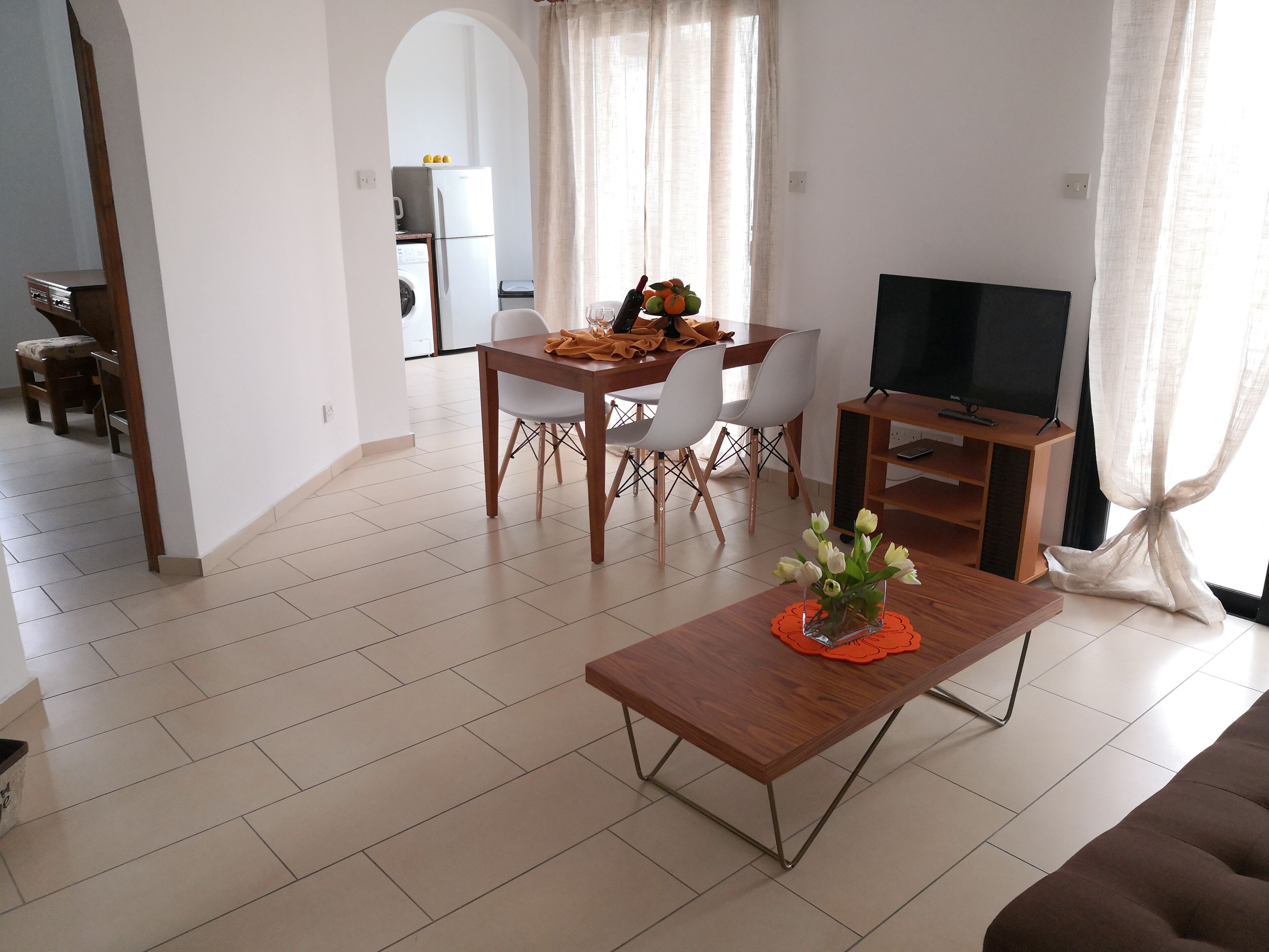 A modern living room with a wooden coffee table, a TV stand, and a dining area with chairs and a table.