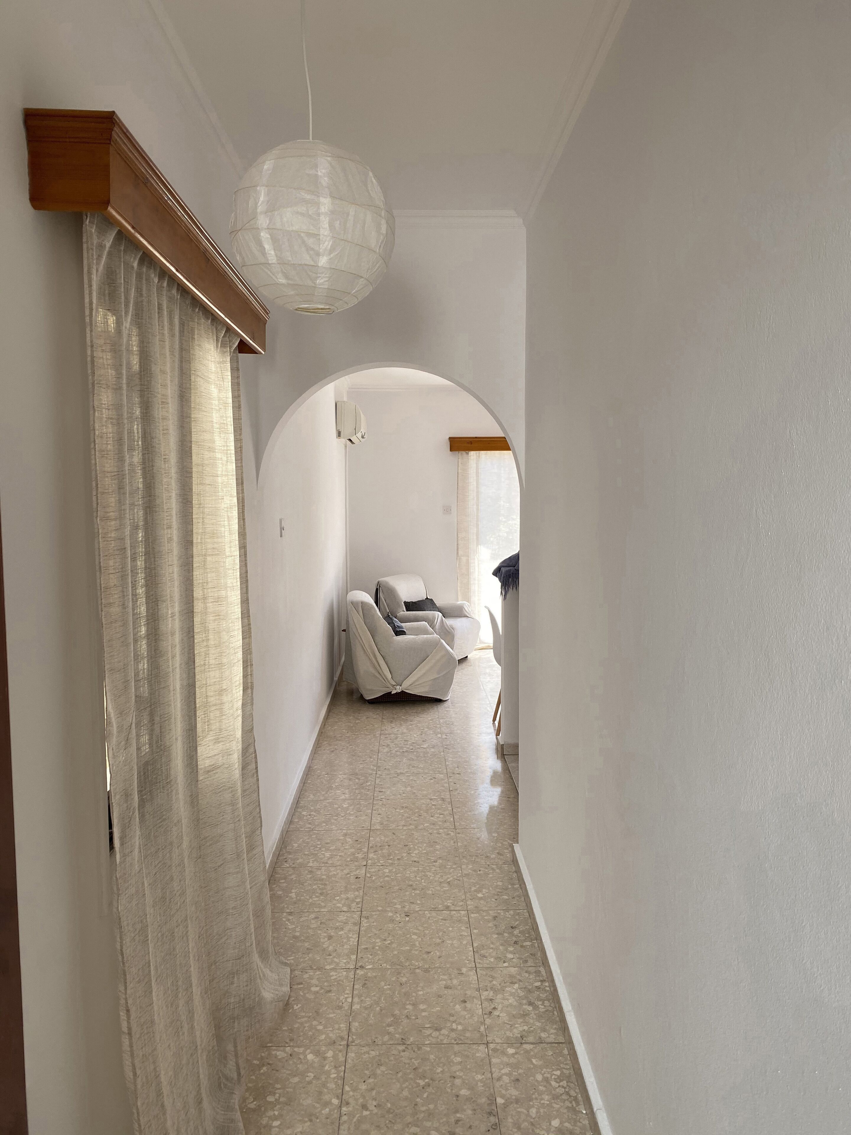 A hallway with a white chair, a hanging light fixture, and a ceiling fan.