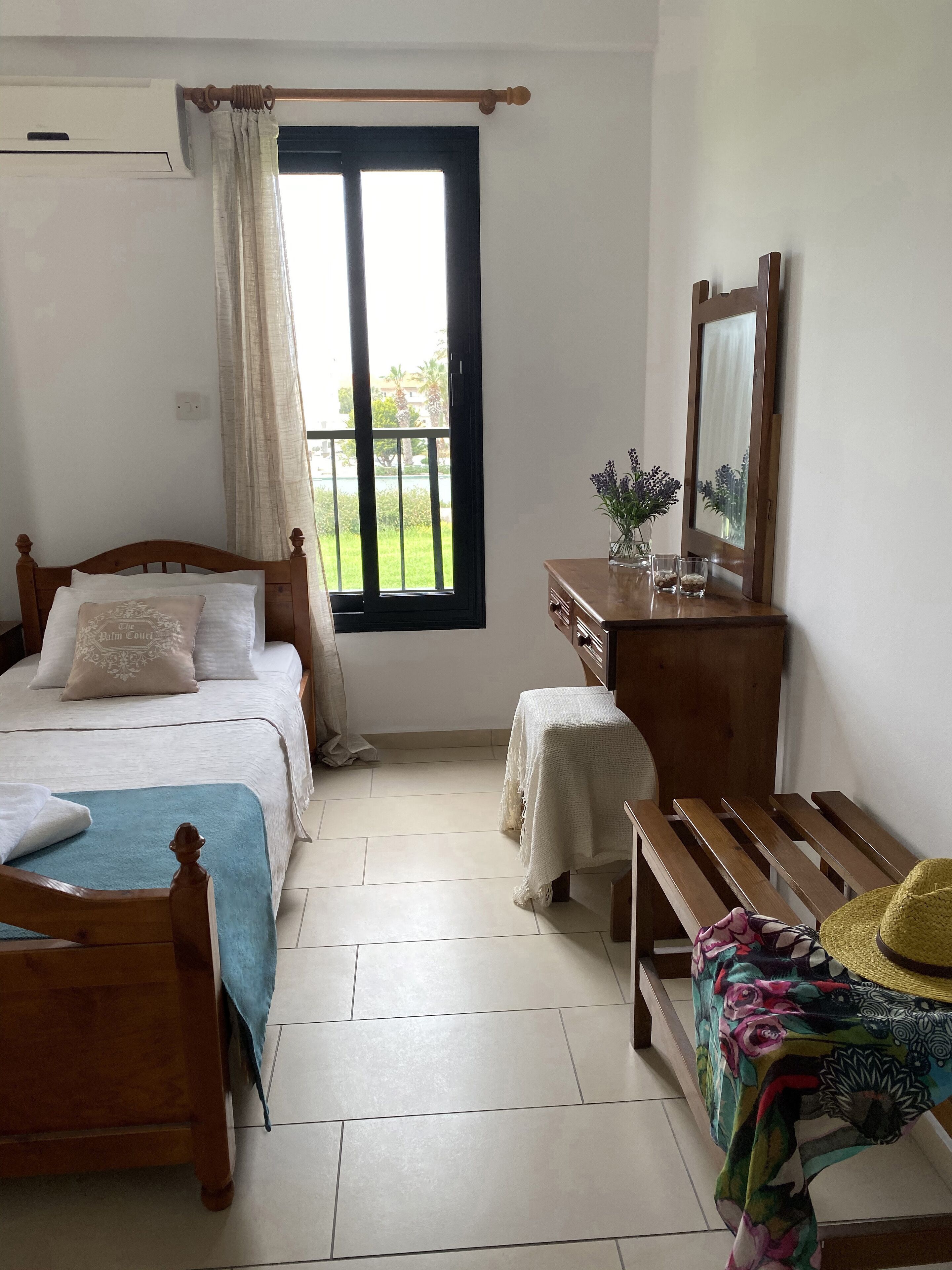 Une chambre à coucher comprenant un lit, un banc en bois, une commode et une fenêtre donnant sur un paysage verdoyant.