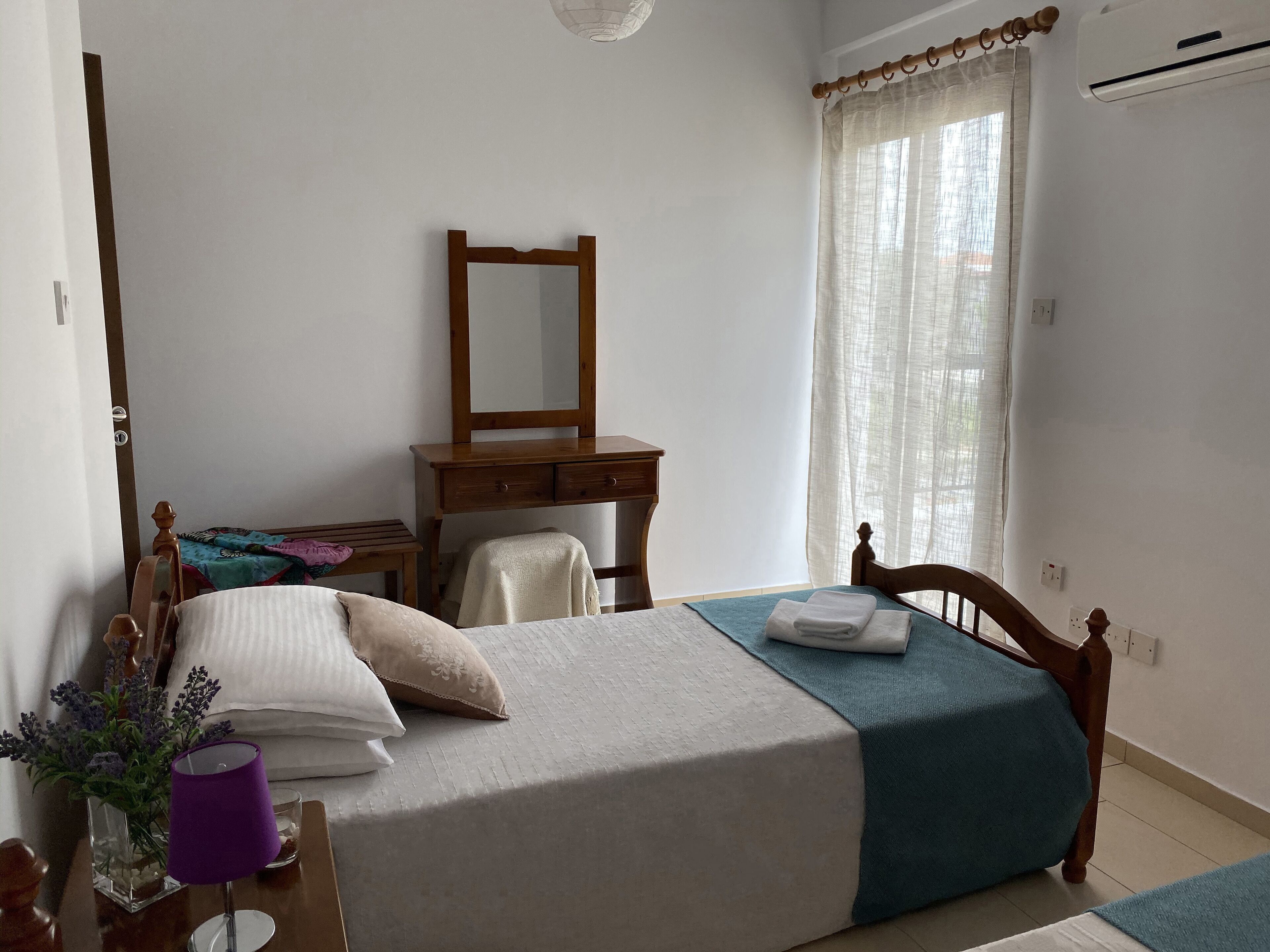 A bedroom with a bed, a wooden desk, a chair, a mirror, and a window with curtains.