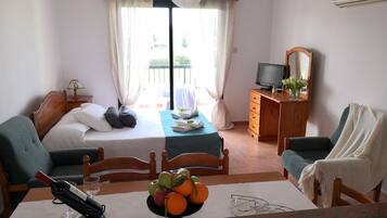 Habitación de hotel con cama, escritorio con computadora, mesa de comedor con fruta y balcón con vistas.