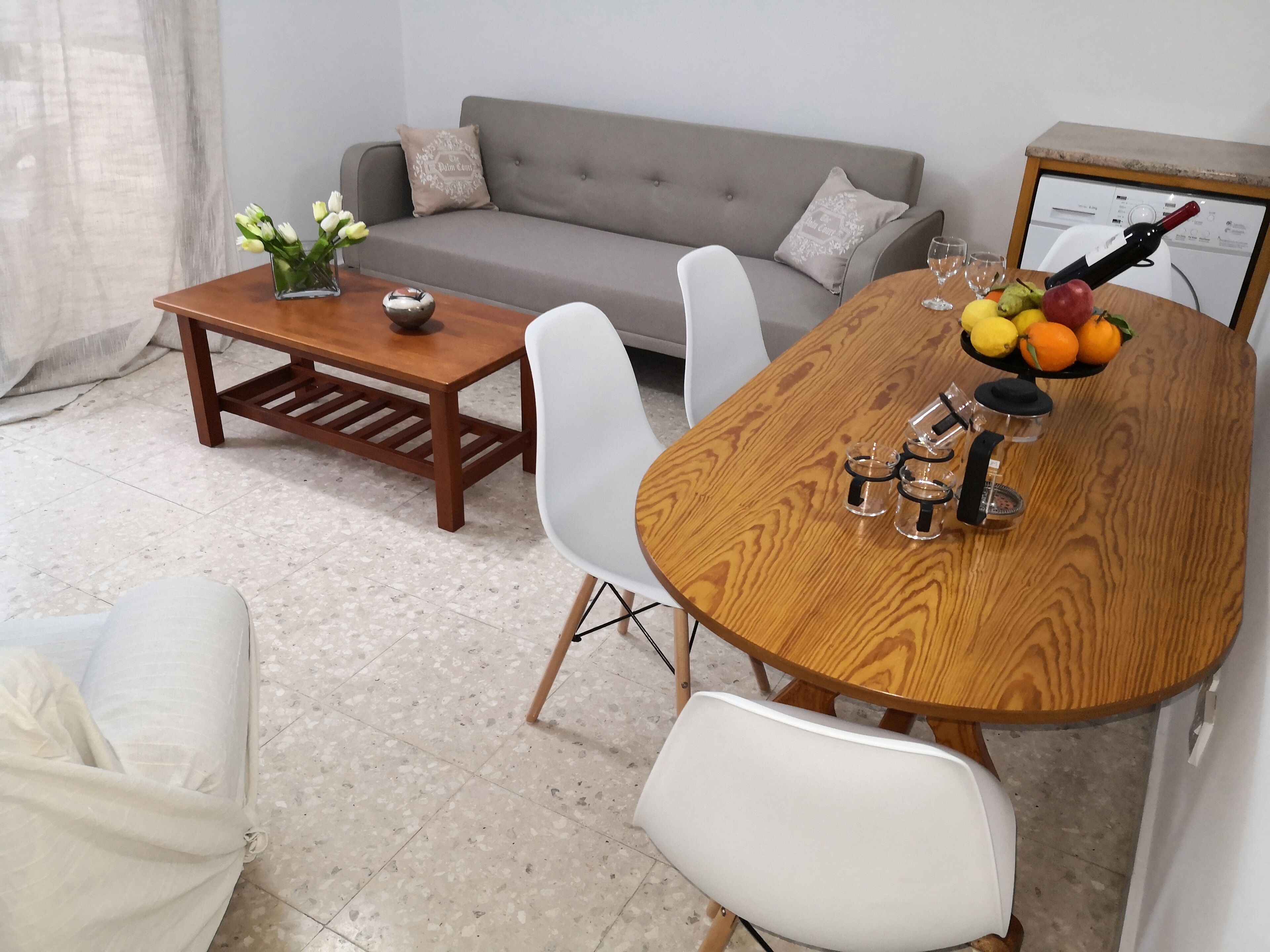 Un coin repas avec une table en bois, des chaises blanches, un canapé gris et un vase de fleurs.