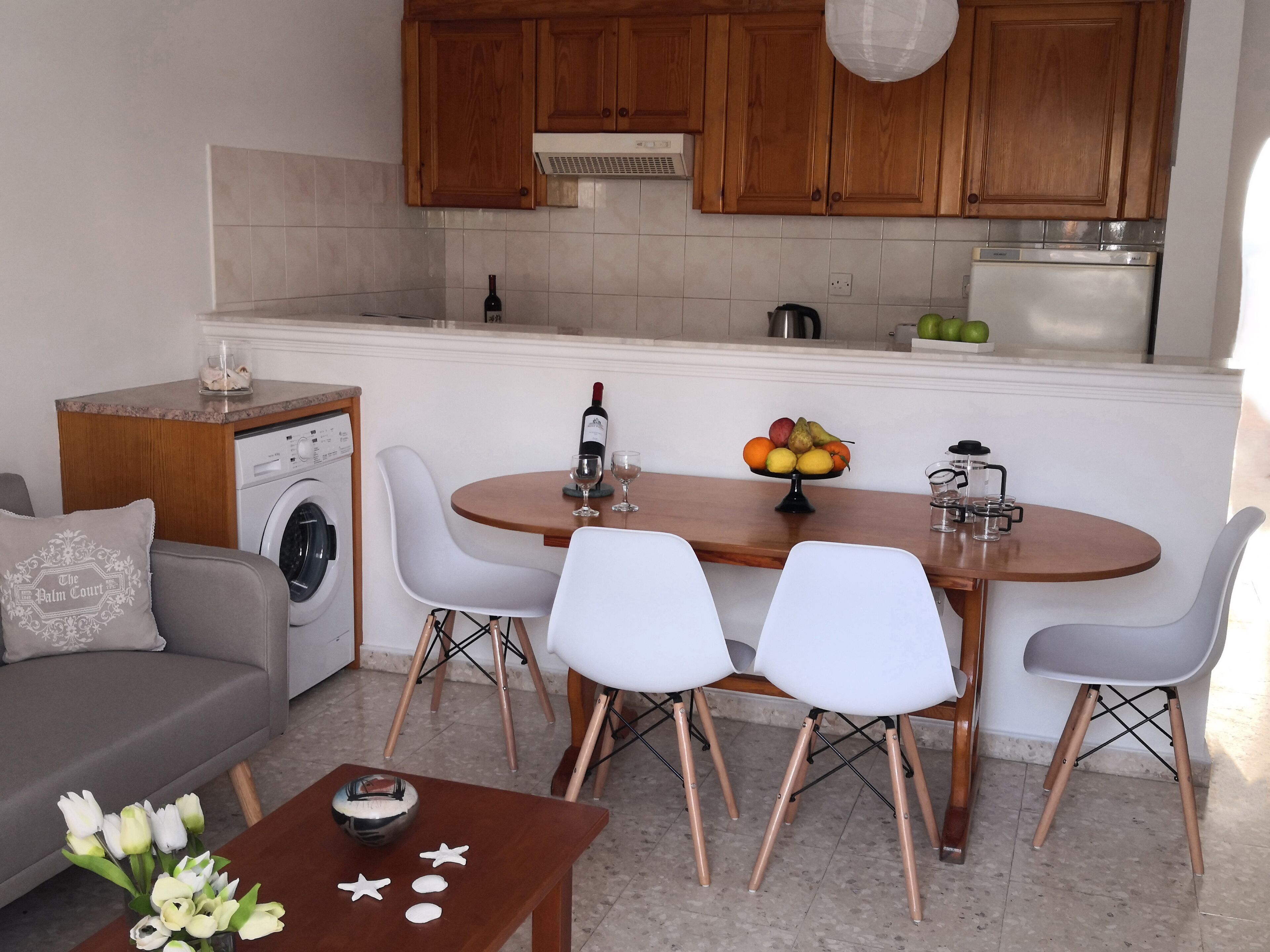 A compact kitchen with wooden cabinets, a built-in washing machine, and a dining area with a round table and white chairs.