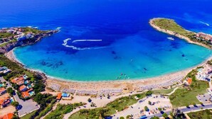 An aerial view of a coastal area with a beach, clear blue waters, and surrounding buildings. - Seashell Apartments (Paphos)