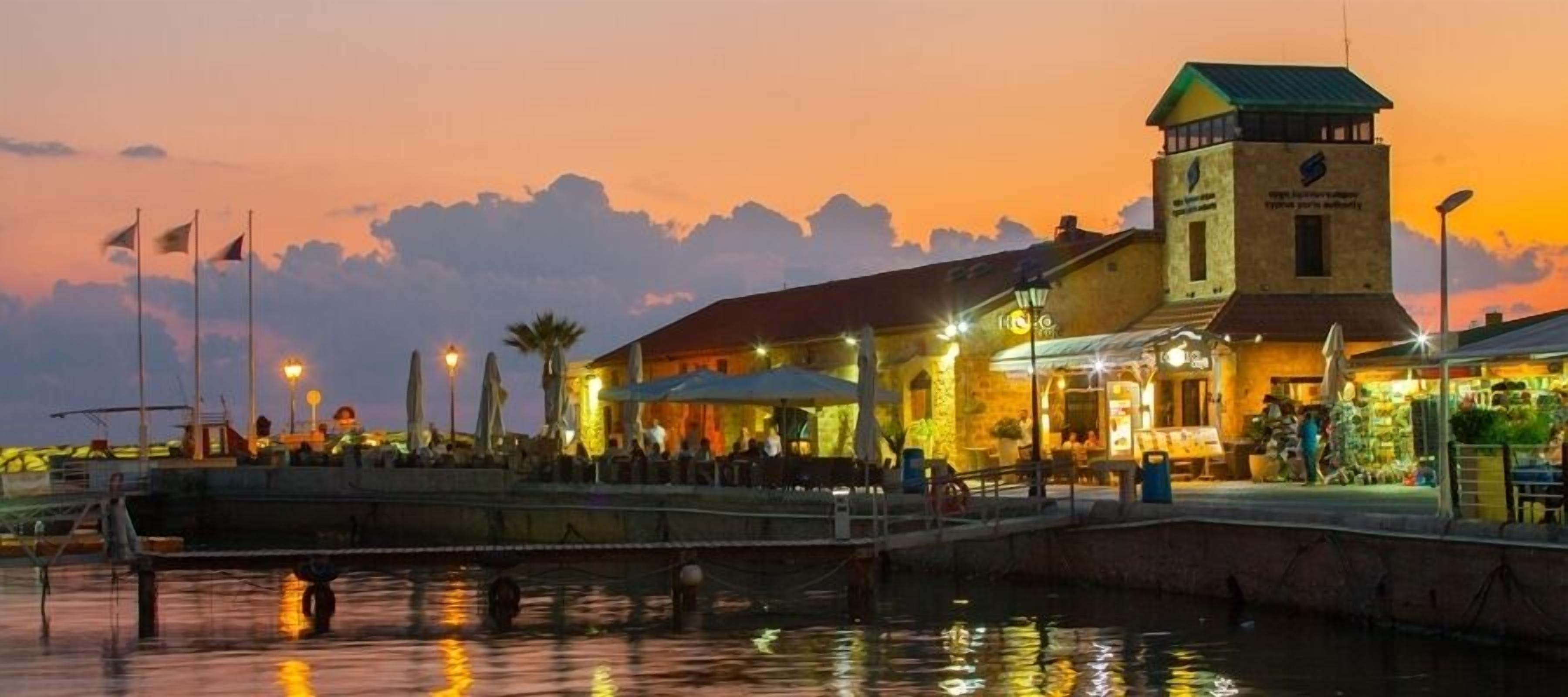 Un edificio frente al agua con torre, mesas al aire libre y un muelle.