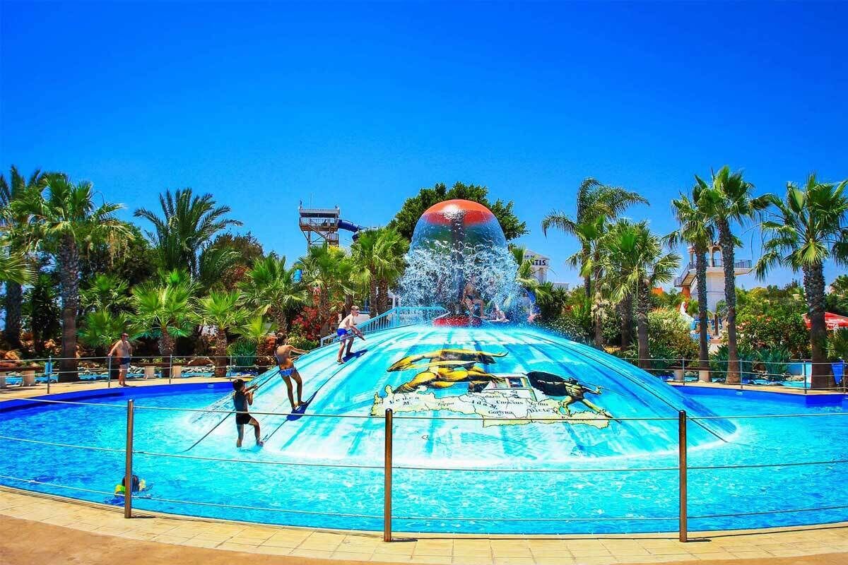 Un toboggan aquatique avec une partie supérieure en forme de sphère, entouré d’une piscine et de palmiers.