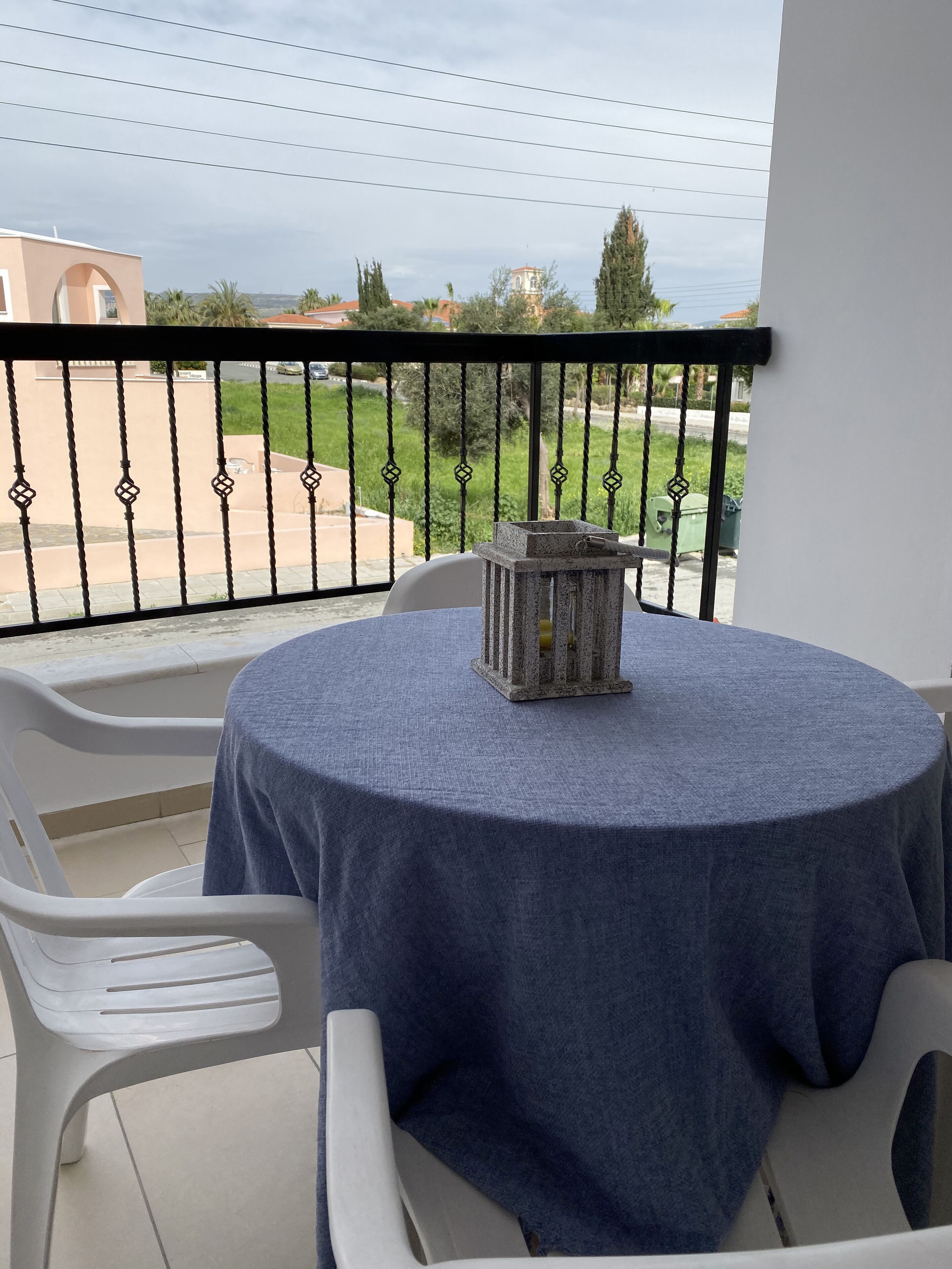 A balcony with a round table covered by a blue tablecloth, two white plastic chairs, and a stone lantern.