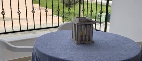A balcony with a round table covered by a blue tablecloth, two white plastic chairs, and a stone lantern.