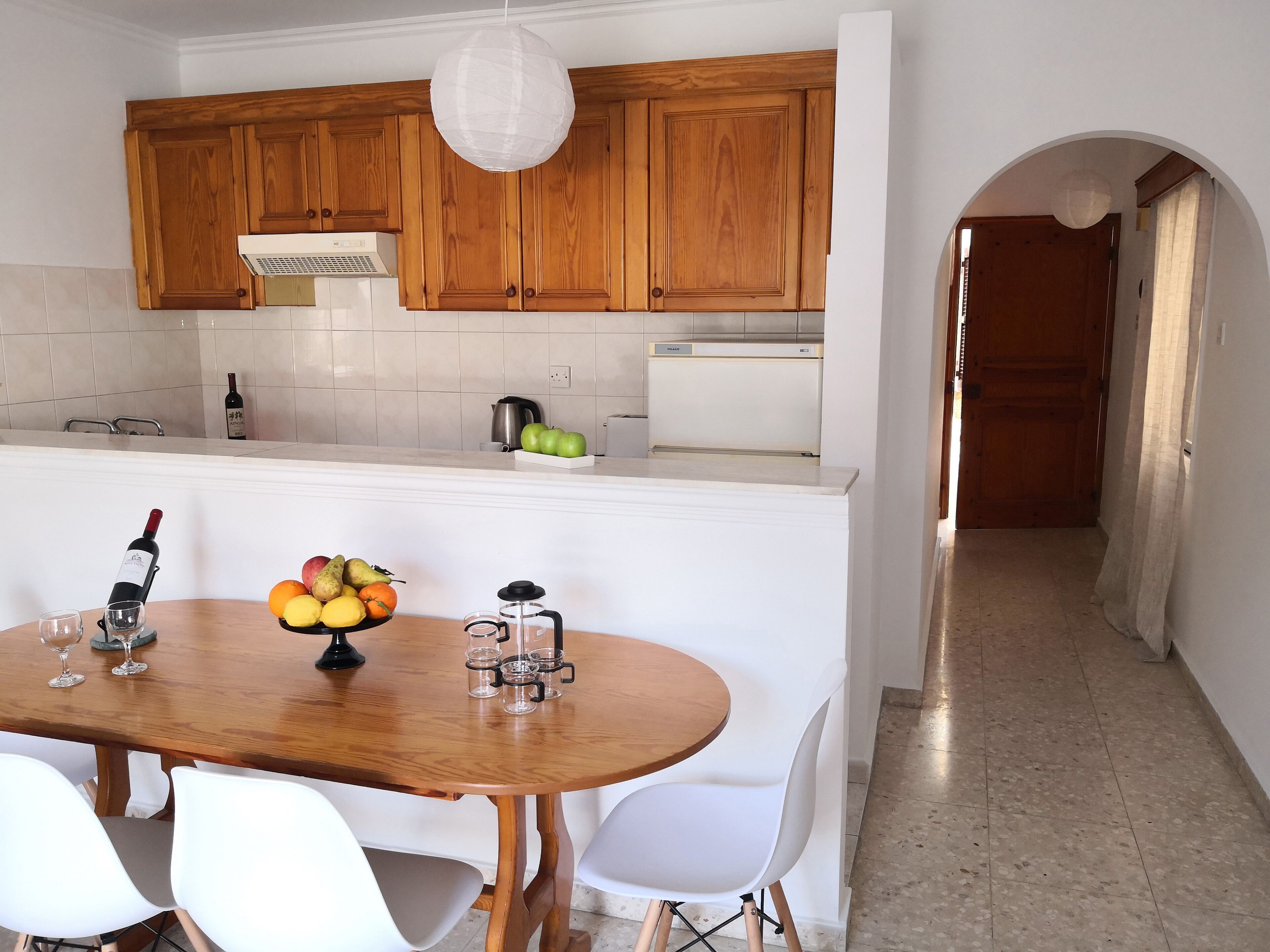A kitchen with wooden cabinets, a white countertop, and a dining area with a wooden table and white chairs.